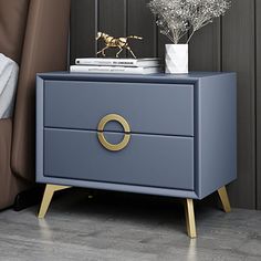 a night stand with two drawers and a gold ring on the bottom, sitting next to a bed