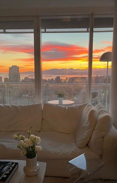 a living room filled with furniture and large windows overlooking the city at sunset or sunrise