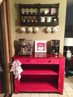 a red cabinet sitting in the corner of a room next to a wall mounted coffee maker