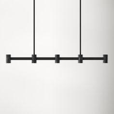 four lights hanging from a black metal bar over a white wall in an empty room