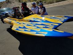 two men are standing next to a yellow and blue surfboard with flames on it