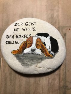 a painted rock with a dog laying on it's side and the words der geist st willig, der kopper chilllig