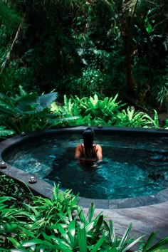 a woman is sitting in the middle of a hot tub surrounded by greenery and trees