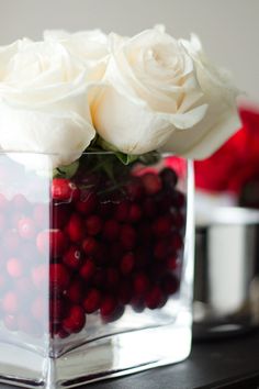 a vase filled with white roses and cranberries on top of a wooden table