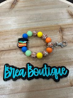 the bead boutique keychain and bracelet are sitting on top of a wooden board