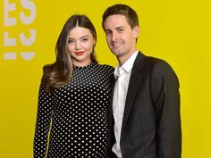 a man and woman standing next to each other in front of a yellow wall with white polka dots