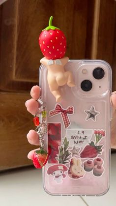 someone is holding up their phone case with a strawberry on the top and other items attached to it