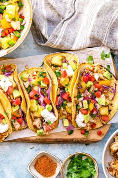 several tacos are lined up on a cutting board next to bowls of salads