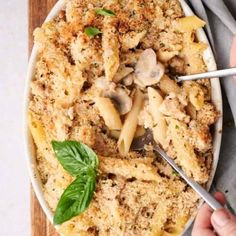 a person holding a spoon in a bowl of pasta with mushrooms and basil on top