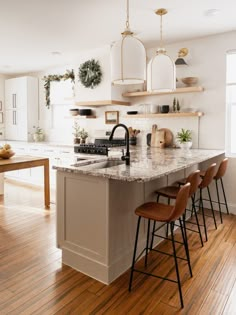 a kitchen with white cabinets and marble counter tops, wooden floors, and hanging lights above the island