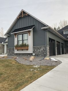 a gray house with two garages and windows on the front side, grass in front of it