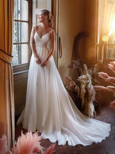 a woman standing in front of a window wearing a wedding dress and posing for the camera