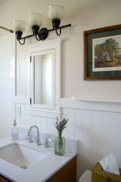 a bathroom sink with two lights above it and a painting on the wall behind it