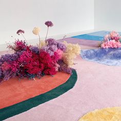 an arrangement of flowers is on the floor in front of a white wall and colorful carpet