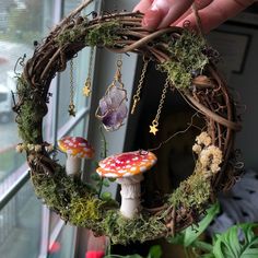 a hand holding a wreath with two mushrooms on it and moss growing in the middle