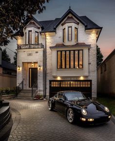 a black sports car parked in front of a large white brick house at night with lights on