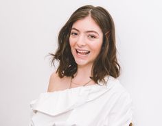 a smiling woman in a white top is looking at the camera and she has brown hair