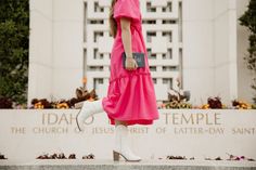 a woman in a pink dress and white boots is standing outside the temple with her hand on her hip