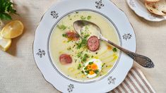 a white plate topped with soup next to slices of lemon and bread on top of a table