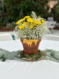 a potted plant with yellow flowers sitting on top of a white tablecloth covered table