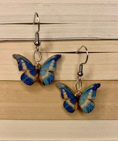 two blue and white butterfly earrings hanging from hooks on a wooden surface with wood planks in the background