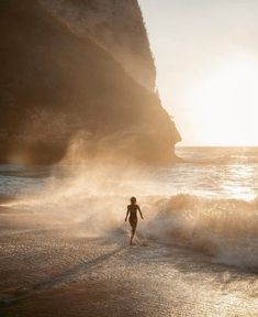 a person is running on the beach in front of an ocean cliff at sunset or sunrise