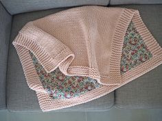 a pink sweater laying on top of a gray couch next to a flowered blanket