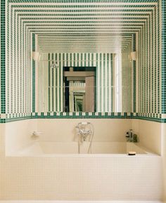 a bathroom with green and white tiles on the wall, tub and mirror in it