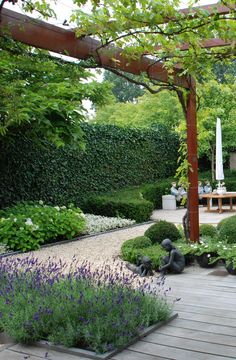 a wooden deck surrounded by lots of plants and flowers in front of a pergolated area