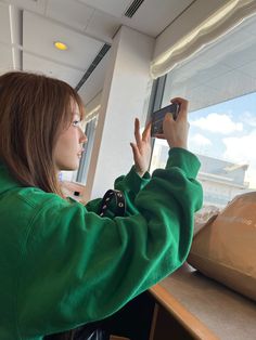 a woman is looking out the window while holding her cell phone up to take a photo