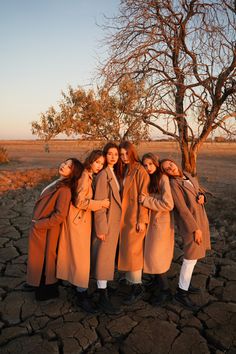 four girls are standing in front of a tree and cracked ground with their arms around each other