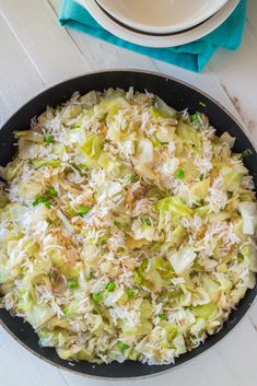 a skillet filled with rice and vegetables on top of a white wooden table next to a bowl of broccoli