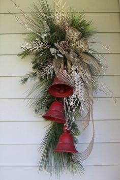 a christmas wreath hanging on the side of a house with bells and pine cones attached to it