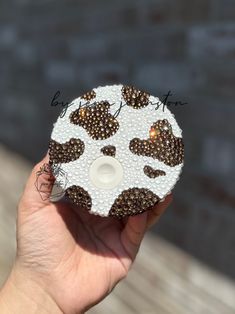 a hand holding a white and brown object with black spots on it's face