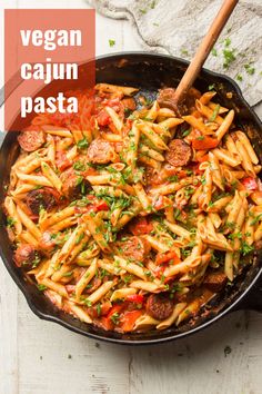 a skillet filled with pasta, sausage and tomato sauce on top of a wooden table