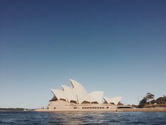 the sydney opera house is seen from across the water, with blue skies in the background