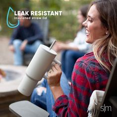 a woman holding a cup while sitting in front of a fire pit with other people