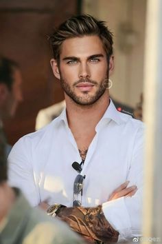 a man wearing a white shirt and tie with tattoos on his arm looking at the camera