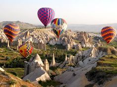 many hot air balloons are flying in the sky over some rocks and trees, with mountains in the background