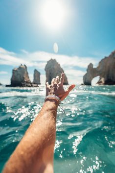 a hand reaching out to the ocean with rocks in the background on a sunny day