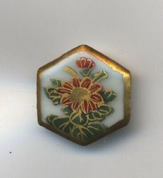 a small white and gold flower broochle on a white surface with red flowers in the center