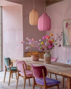 a wooden table topped with pink chairs next to a vase filled with flowers