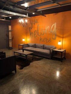 a living room with two couches and a coffee table in front of an orange wall that says, you belong here