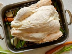 a metal basket filled with raw chicken and carrots next to celery leaves