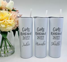 three white tumblers with the words girls weekend on them next to a bouquet of flowers