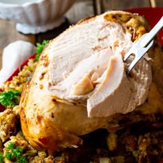 a turkey is being cut with a knife on top of stuffing in a red dish