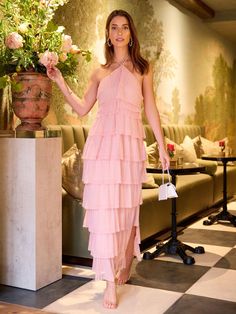 a woman in a pink dress standing next to a flower pot and holding a white purse