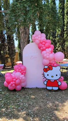 a hello kitty balloon arch in the middle of a field with pink balloons on it