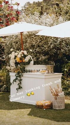 an outdoor bar with flowers and lemons on the table under an umbrella in front of some bushes