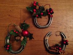 three christmas wreaths made out of horseshoes on a wooden floor with pine cones and berries